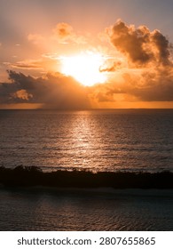 Sun breaks through towering cumulus clouds near Dhigurah Island, Maldives, casting a golden path on calm water, with a thin island silhouette and soft reflections.