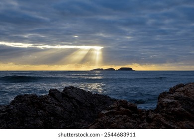 the sun bursting through the clouds before setting over the ocean