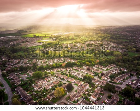 Sun bursting through clouds over traditional British houses with countryside in the background. Dramatic lighting and warm colours to give a homely effect.