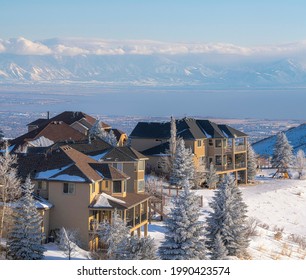 The sun is casting its light on two huge houses without people outside. There is snow all around the yellow property. There are ranges of mountains behind the houses.