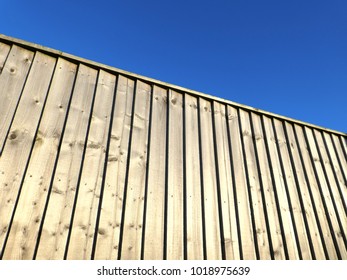 The Sun Casts Shadows On Wooded Fencing Panels Against Blue Sky