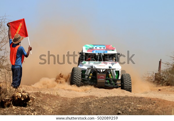 Sun City, South Africa - OCTOBER 1, 2016: Front view of\
white Bat rally car stopped by marshal with red flag at road\
crossing in race at Sun City 450 Rally Racing event, Sun City,\
South Africa  
