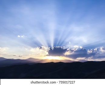 The sun is coming out from behind a cloud, over the mountains . Blue sky and sunshine