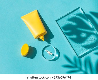 Sun cream yellow tube on the blue wet background with tropical leaves shadows. Summer vacation cosmetics concept. Top view