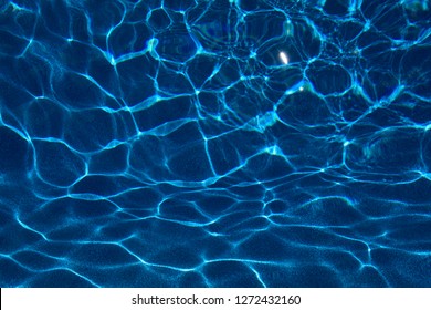 Sun creating abstract dappled light mesh from waves on a blue pool
