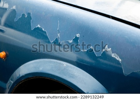 Sun damaged, faded, and peeling blue paint on a car's front fender. Close up shot, no people.