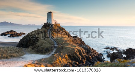 The sun descends behind Twr Mawr Lighthouse on an isolated beach on Anglesey, Wales.