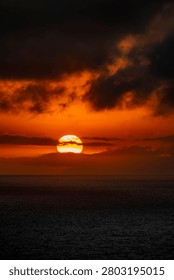 The sun dips below the horizon, casting a vibrant orange glow across the sky and reflecting on the dark, rippling ocean surface