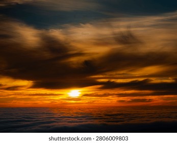 The sun dips below the horizon, casting a warm glow across a vast expanse of clouds, creating a breathtaking natural spectacle