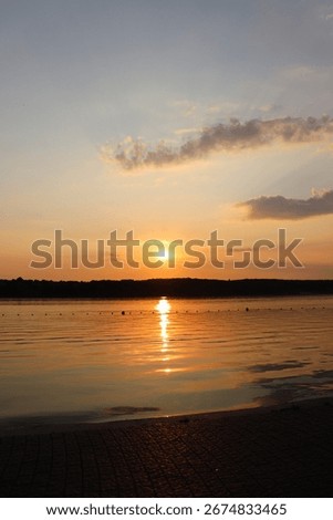 The sun dips below the horizon, casting a brilliant orange and golden glow over the tranquil lake. A perfect, peaceful sunset scene.
