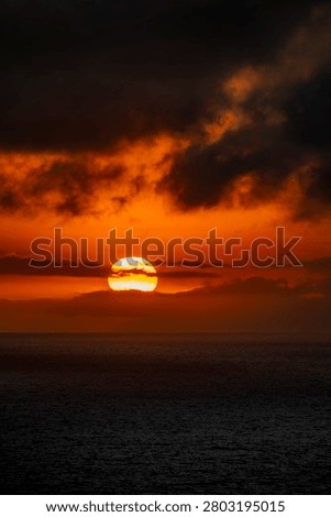 The sun dips below the horizon, casting a vibrant orange glow across the sky and reflecting on the dark, rippling ocean surface
