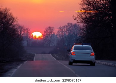 the sun dips below the horizon over the road and police car