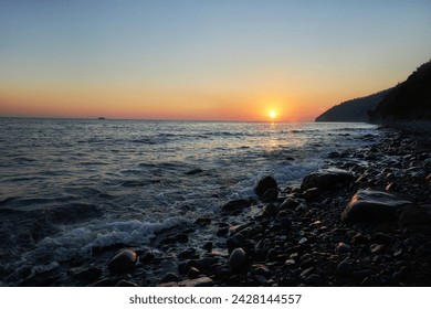 Sun dips below horizon, rocky coastline, nature beauty in serene tranquility. Waves gently lap against shore, while silhouetted cliffs stand majestically against dusky sky - Powered by Shutterstock