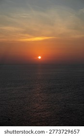 Sun dips below ocean's edge, painting sky in amber and blue. Water reflects the glow, calm and vast. Soft clouds drift above, gently illuminated. This moment captures serene transition, quiet beauty