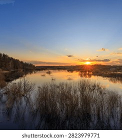 Sun dips low over calm lake, painting sky in gold and soft blue. Reflections ripple gently