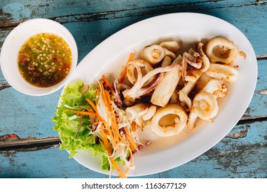 Sun dried calamari or fried squid with chilli sauce (seafood sauce). Thailand Food Style on the white plate over wooden table