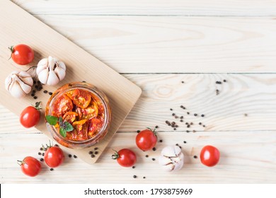Sun dried tomatoes in glass jar with ripe tomatoes and garlic on cutting board, on wooden background, top view, copyspace - Shutterstock ID 1793875969
