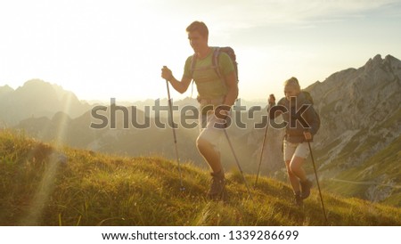 SUN FLARE: Happy Caucasian woman and man enjoying a morning hike in the stunning mountains of Slovenia. Carefree tourist couple having fun trekking in the tranquil Alps on a sunny summer afternoon