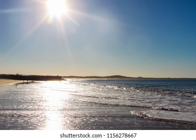 Sun flare on water in late afternoon with unrecognizable people in the distance - Noosa Heads Australia