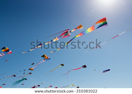 Sun flare and rays shine over colorful kites flying against a blue sky