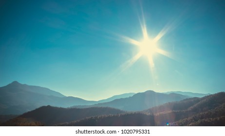 Sun flare shining over a solid blue sky and mountain landscape