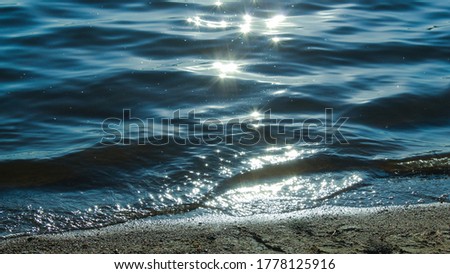 Sun glare in waves of sea water on a tropical beach in summer in nature close-up. Beautiful texture of water waves.Sea wave and sand seashore. Golden sun light over the sea ocean waves