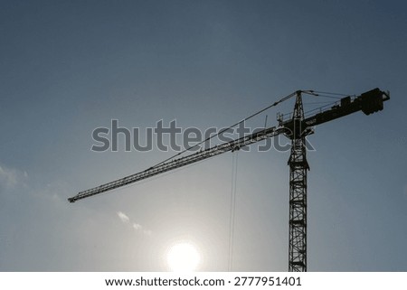 Sun glints behind the structure's metal frame. Construction work continues amid daylight. Workers unseen, but presence implied