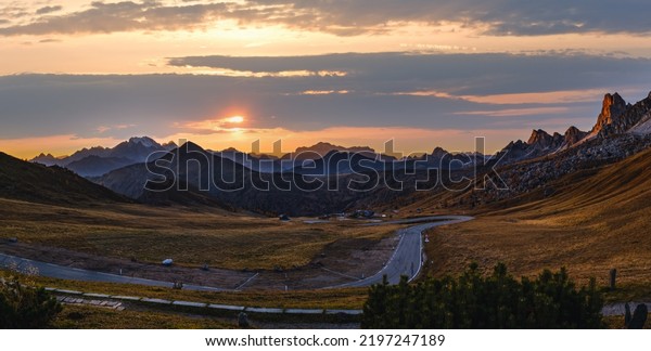 Sun glow in\
evening hazy sky. Italian Dolomites mountain silhouettes panoramic\
peaceful view from Giau Pass. Climate, environment and travel\
concept scene. Cars\
unrecognizable.