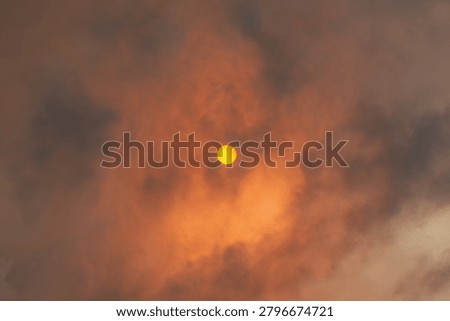 The sun glows orange through dense wildfire smoke and dramatic clouds, creating an intense atmospheric sky.