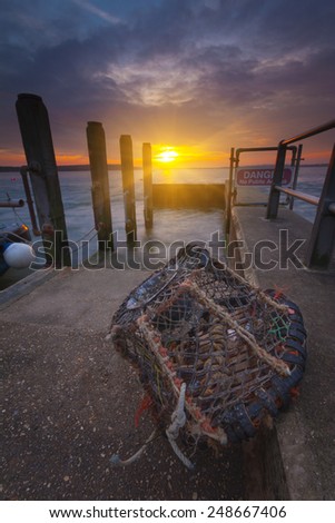 The sun goes down over a lone lobster pot by a slipway