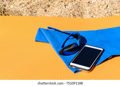 Sun goggles lying on a microfiber towel next to the mobile on the travel Mat which is on the beach