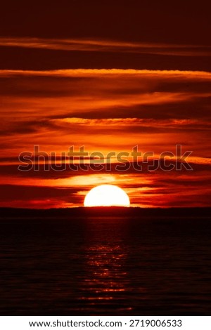 A sun, half set,  on a sunset sky illuminating the 