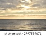 The sun hides behind drifting clouds, leaving the ocean wrapped in gentle, fading warmth.
