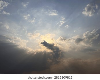 The sun hides behind soft clouds, creating a gentle glow across the sky. Rays of golden light spread around the cloud edges, forming a peaceful and beautiful scene. The cloudy atmosphere adds mystery and calmness to the natural landscape.
