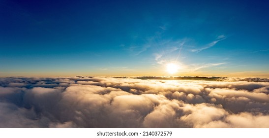 Sun light shining brightly on blue sky above thick layer of white fluffy clouds at sunrise with mountains on background panorama view