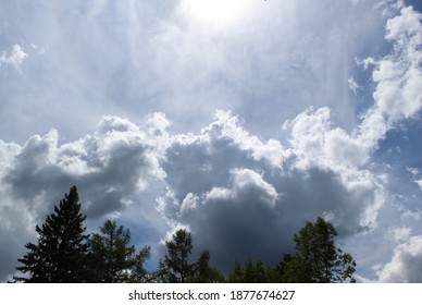 Sun light shining down on large mountains of white billowing clouds with tree line along bottom.
