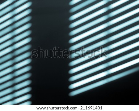 Sun lights and shadow on a room wall from a window roller shutter - cool cyanotype