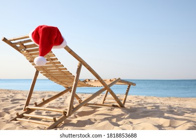 Sun Lounger With Santa's Hat On Beach, Space For Text. Christmas Vacation