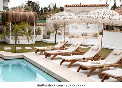 Sun loungers and parasols poolside. Poolside decoration ideas. Sunbathing by the pool in the beautiful hotel garden, no people.