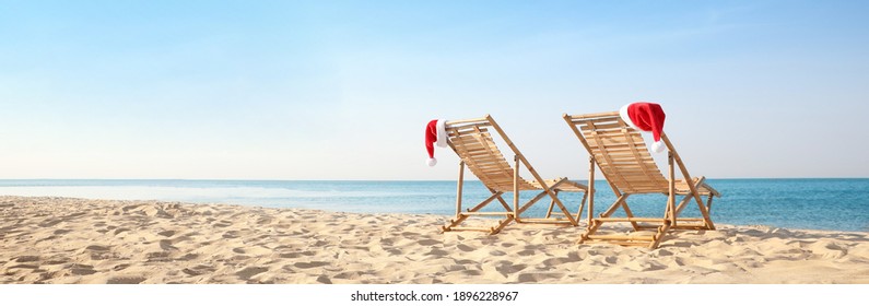 Sun loungers with Santa's hats on beach, banner design. Christmas vacation - Powered by Shutterstock