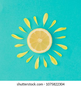 Sun made of lemon and yellow flower petals on bright blue background. Fruit summer minimal concept.