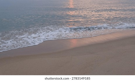 Sun path reflection on calm ocean surface at dawn.
Golden sun road reflecting on the sea water surface with a soft white wave approaching the sandy beach.