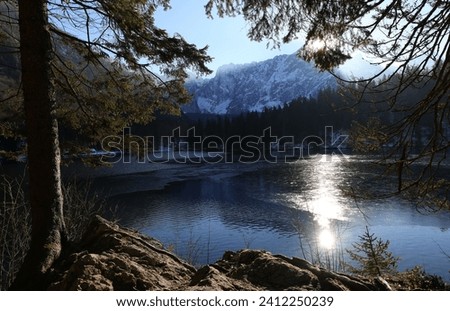 sun peeking behind the mountains and the reflection of the mountains on the beautiful alpine lake in winter