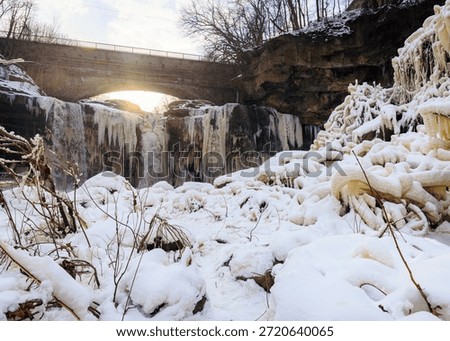 The sun peeks through the bridge over a partially frozen Western Falls of Cascade at Cascade Park in Elyria, Ohio during winter.