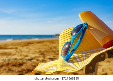 Sun Protection Accessories On Sea Shore. Blue Sunglasses, Yellow Straw Hat And Sunscreen Lotion On Sandy Beach. Summer And Holidays.