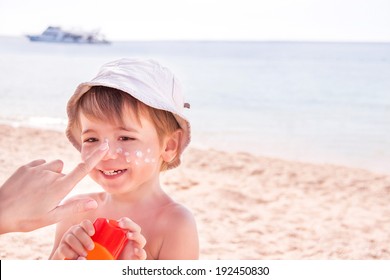 Sun protection. Hand of caucasian mother applying suncream  (suntan lotion) from a plastic container to her happy son before tanning during summer holiday on beach.  Copyspace, close up. - Powered by Shutterstock