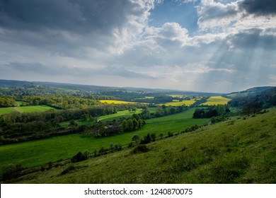 Sun rays break through clouds with view of Surrey Hills with yellow rape fields in Springtime.
