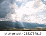 Sun rays breaking through clouds, illuminating a lush valley and mountains