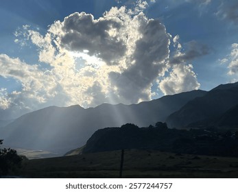 Sun rays breaking through clouds over a mountain range, creating a dramatic and serene landscape.