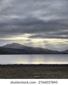 Sun rays breaking through clouds over mountain lake landscape